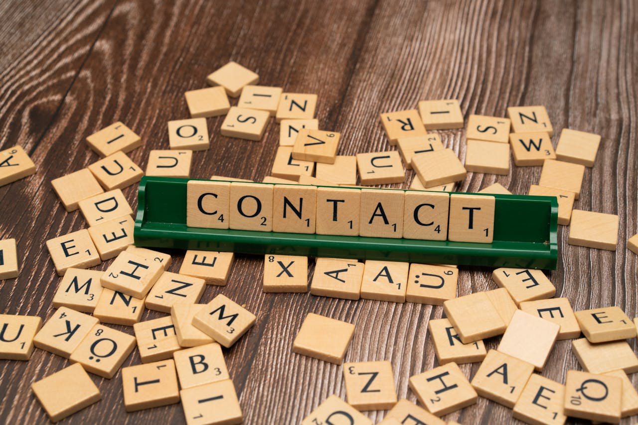 Scrabble tiles spelling CONTACT on a wooden surface with scattered tiles around.